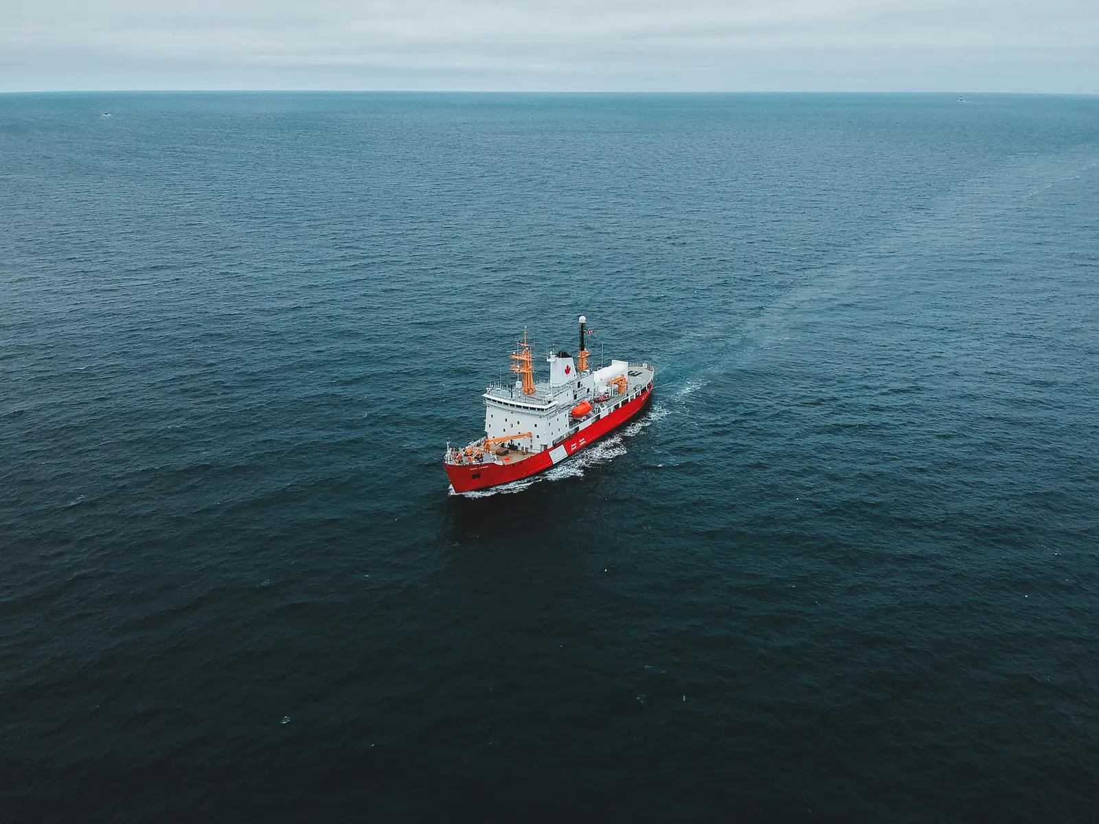Embarcación de trabajo roja navegando mar adentro bajo un cielo cubierto
